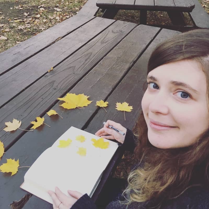 Molly Murphy at wooden table with fallen leaves looking at camera with her writer's journal